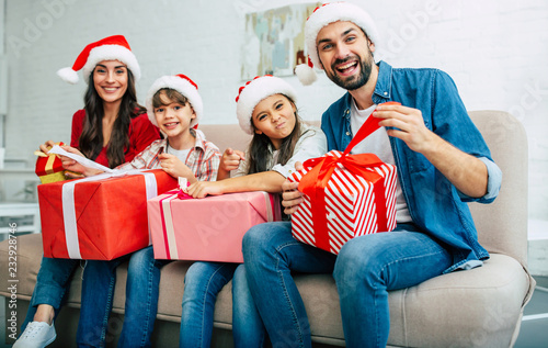 Big happy and cheerful family in santa hats giving christmas presents in living room while New Year holidays