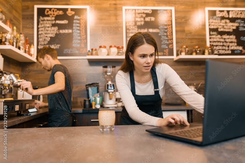 Young couple man and woman owners of small modern coffee house using laptop computer for work