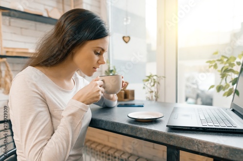 Young female blogger in coffee shop with laptop computer and cup of fresh coffee