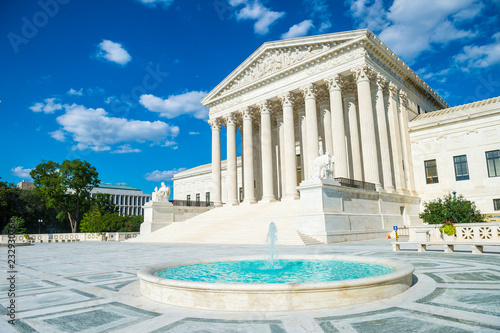 Bright scenic view of the neo-classical facade of the United States Supreme Court building from the plaza fountain under blue sky