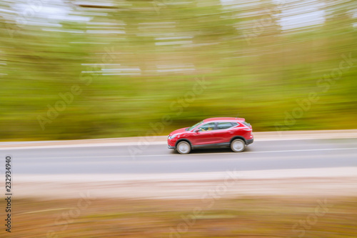 Fast moving red car on asphalt road. Panning shot, blurred background.