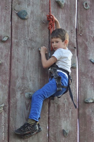 Boy climbing on the wall. Mountaineer in the harness.