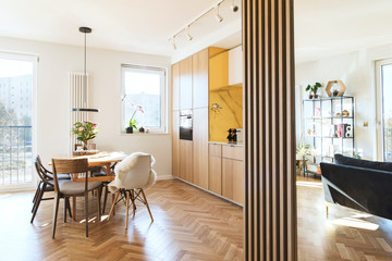 Stylish scandinavian open space with dining and living room with design sofa and family table. Bright and sunny room with big windows and brown wooden parquet.	