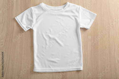 White t-shirt on wooden background, top view