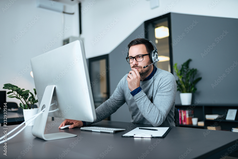 Concerned male customer support operator working in his office. Concerned male customer support operator working in his office.