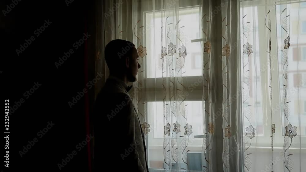 Young businessman puts on and straightens jacket by the window. Young businessman puts on and straightens jacket by the window.