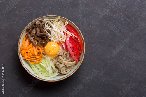 Traditional Asian Bibimbap dish with rice and vegetables on dark background