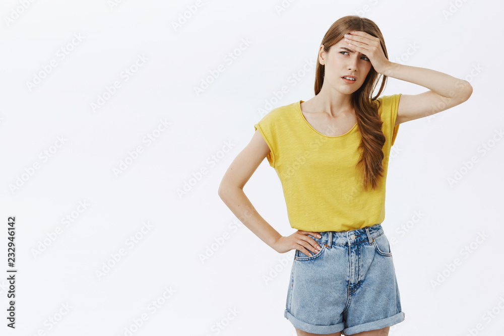 Give me break. Portrait of tensed displeased and bothered good-looking female in yellow t-shirt and shorts holding hand on forehead frowning looking tired left with dissatisfaction