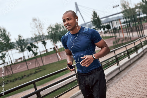 Side view of young active african man with headphones jogging outdoors