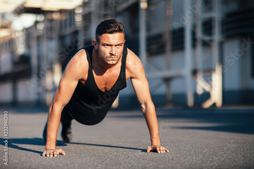 Young serious man doing pushups outdoor on industrial background