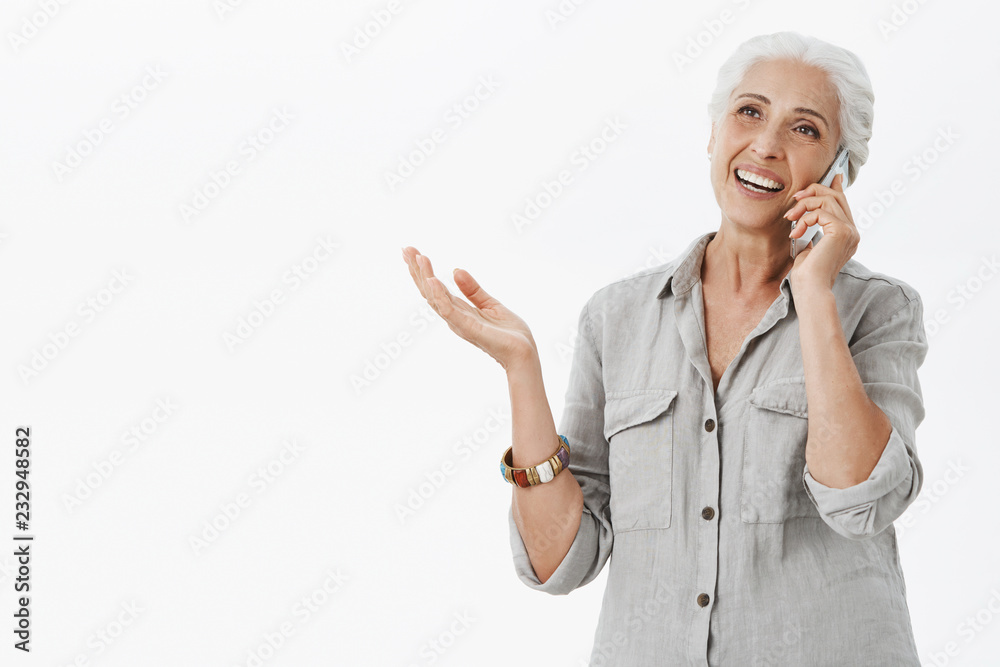 Waist-up shot of delighted caefree kind grandmother talking on telephone and gesturing while being excited and carried away with conversation gazing left holding smartphone near ear Waist-up shot of delighted caefree kind grandmother talking on telephone and gesturing while being excited and carried away with conversation gazing left holding smartphone near ear