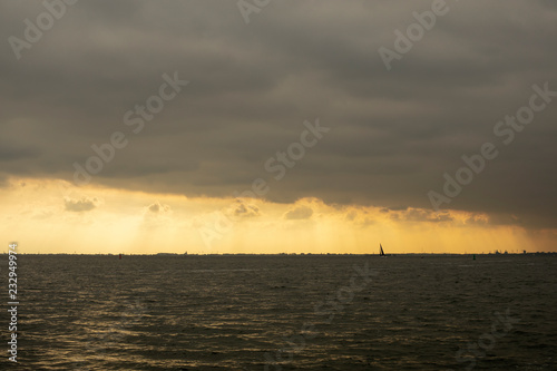 Sailing boat silhouette in front of the skyline of Amsterdam in Holland while the sun is going down and a large cloudy sky.