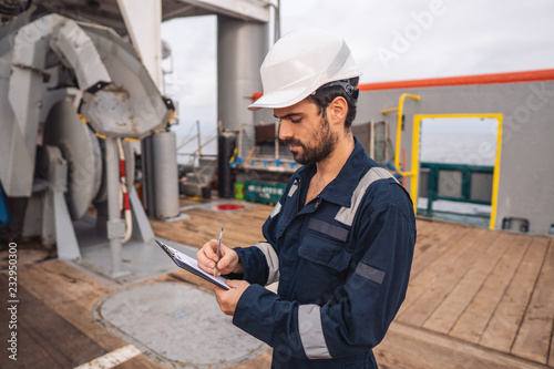 Marine Deck Officer or Chief mate on deck of vessel or ship . He is inspecting and writing checklist. Ship paperwork photo