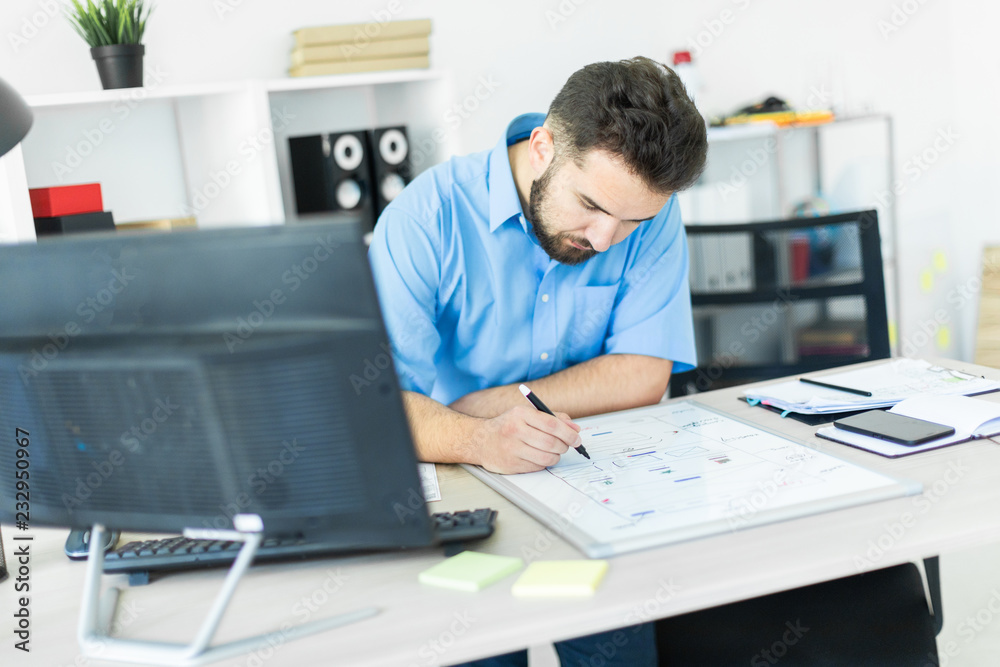 A young man standing in the office at a computer Desk and working with a magnetic Board.