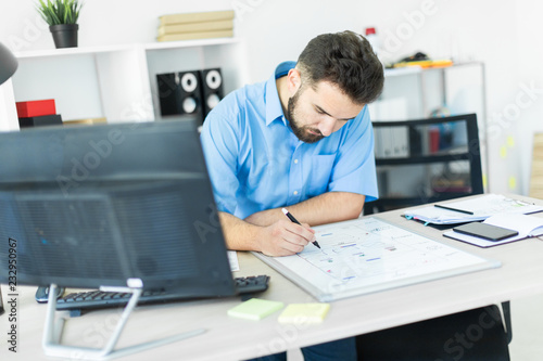 A young man standing in the office at a computer Desk and working with a magnetic Board.