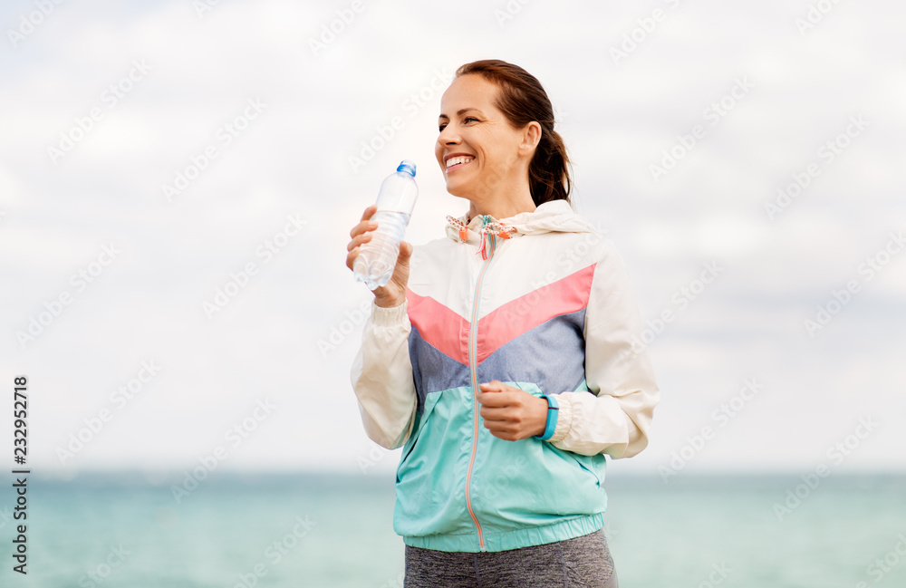 fitness, sport and healthy lifestyle concept - woman drinking water after exercising at seaside fitness, sport and healthy lifestyle concept - woman drinking water after exercising at seaside