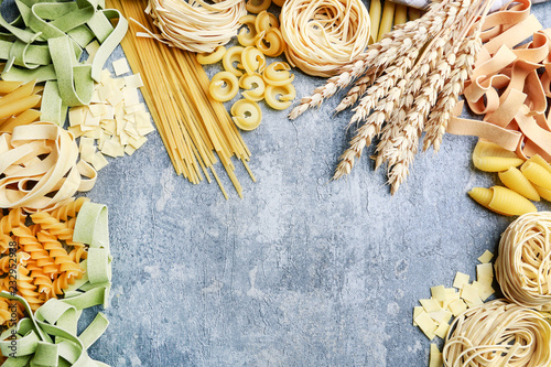 Mixed types and shapes of italian pasta on grey stone, background photo