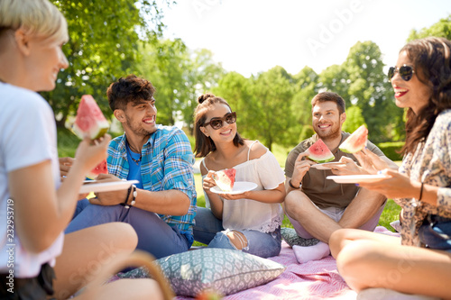 friendship  leisure and food concept - group of happy friends eating watermelon at picnic in summer park