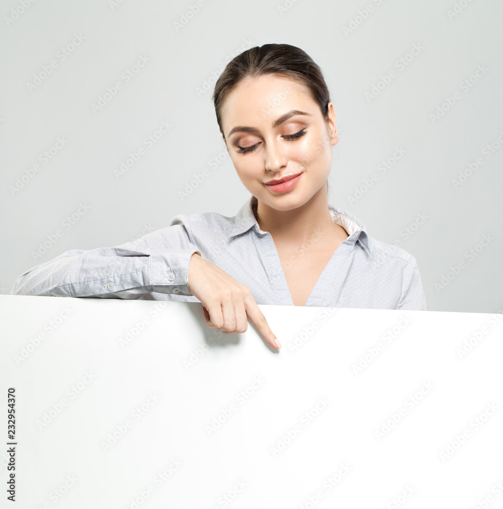 Friendly young woman pointing and holding white empty signboard paper background. Happy student girl Friendly young woman pointing and holding white empty signboard paper background. Happy student girl