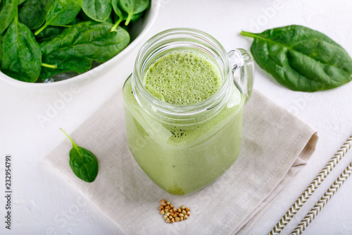 Green smoothie drink in glass jar on white. Mixed cocktail with spinach and green buckwheat.