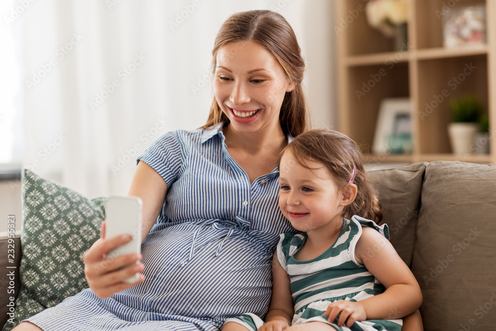pregnancy, people and family concept - happy pregnant mother and little daughter with smartphone at home pregnancy, people and family concept - happy pregnant mother and little daughter with smartphone at home