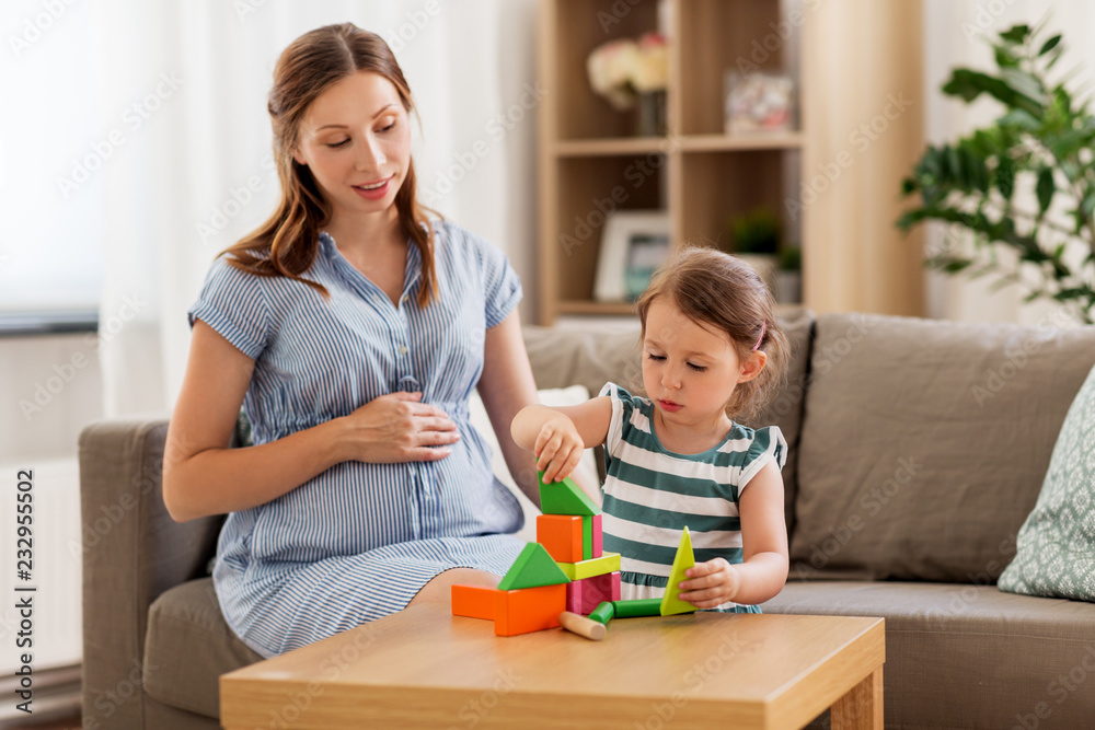 childhood and people concept - happy pregnant mother and little daughter playing with toy blocks at home childhood and people concept - happy pregnant mother and little daughter playing with toy blocks at home