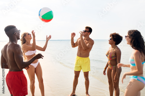 friendship, summer holidays and people concept - happy friends playing with inflatable ball on beach