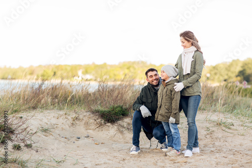 family, leisure and people concept - happy mother, father and little daughter at autumn beach