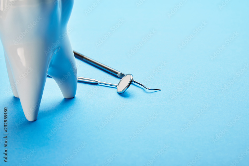 close up view of sterile dental mirror, probe and tooth model arranged on blue backdrop