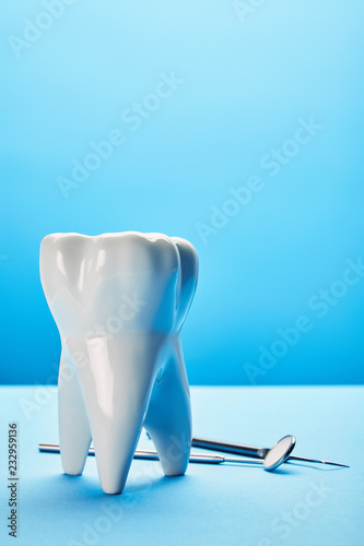 close up view of sterile dental mirror  probe and tooth model arranged on blue backdrop