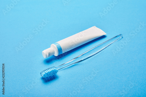 close up view of toothbrush and toothpaste arranged on blue backdrop, dentistry concept