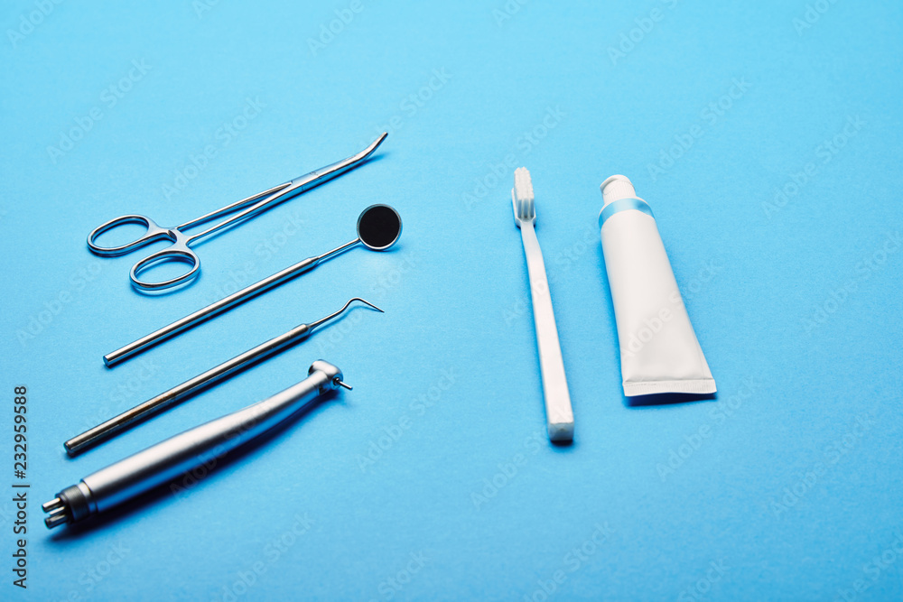 Fototapeta premium close up view of arrangement of sterile dental instruments, stethoscope, toothbrush and toothpaste on blue backdrop, dental care concept