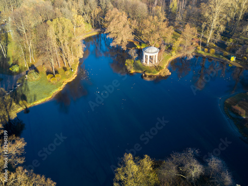 Aerial; drone view of autumn morning in beautiful city park; rest and recreation area with lake and ducks; tall trees with long shadows; pretty stone house on the shore of the pond, Saint Petersburg photo