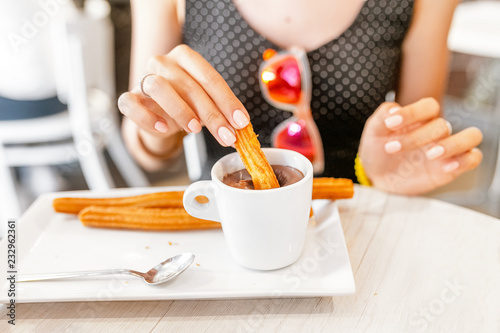 Happy Cheerful girl in hat eating traditional spanish delicious churros, a fried pastry with chocolate in cafe in spain