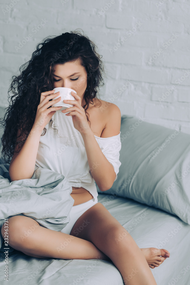 attractive curly woman drinking coffee in bed during morning time at home attractive curly woman drinking coffee in bed during morning time at home