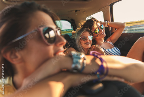 Three female friends enjoying traveling in the car. Sitting in rear seat and having fun on a road trip.