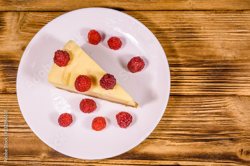 White plate with cheesecake New York and raspberries on wooden table. Top view