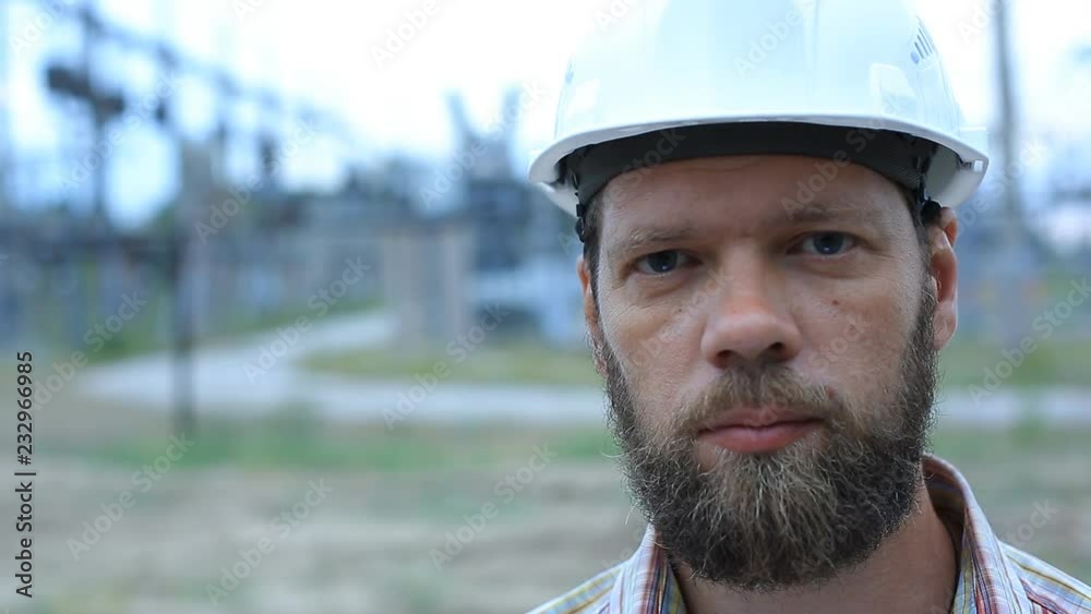 Station technical director with working drawings at nuclear power station. Worker in white helmet with engineering drawing near outdoor switchgear at nuclear power station Station technical director with working drawings at nuclear power station. Worker in white helmet with engineering drawing near outdoor switchgear at nuclear power station