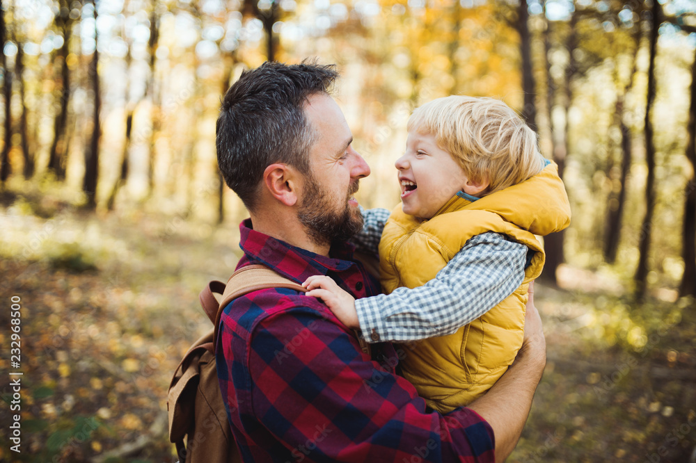A mature father holding a toddler son in an autumn forest, talking. A mature father holding a toddler son in an autumn forest, talking.