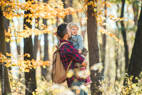 A mature father holding a toddler son in an autumn forest, walking.