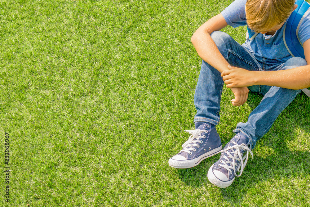 Unhappy sad upset boy sitting alone on the grass Unhappy sad upset boy sitting alone on the grass