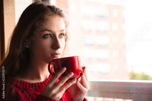 Woman with cup of coffee or tea near window close-up