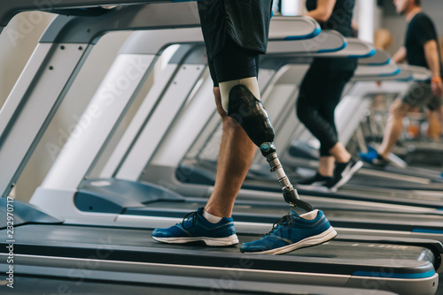 cropped shot of man with artificial leg walking on treadmills at gym with other people