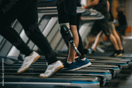 cropped shot of sportsman with artificial leg running on treadmill at gym with other people