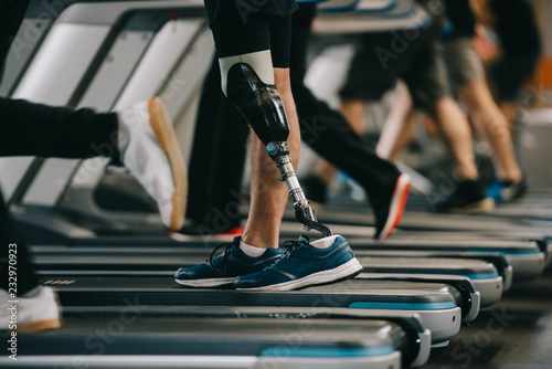 cropped shot of sportsman with artificial leg running on treadmill at gym with other people