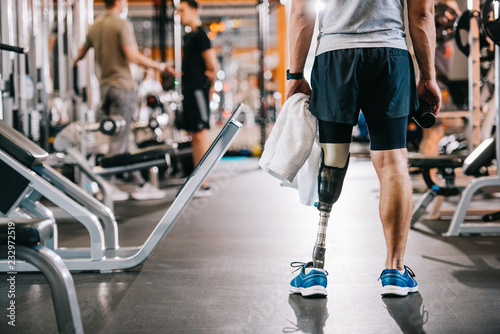 cropped shot of sportsman with artificial leg standing at gym and holding towel