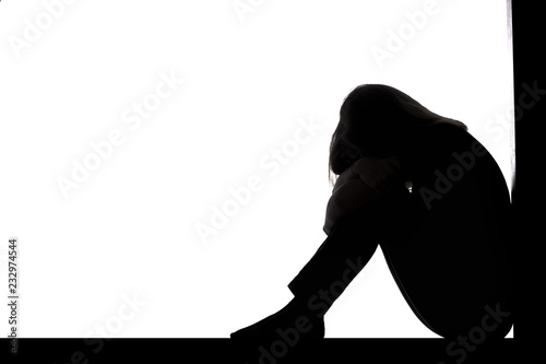 silhouette of a woman sitting on the floor in a corner on a white isolated background, a sad girl crying putting head on knees