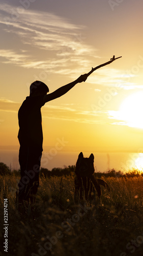 silhouette of a young man playing with a dog in a field at sunset, boy throwing a wooden stick on nature