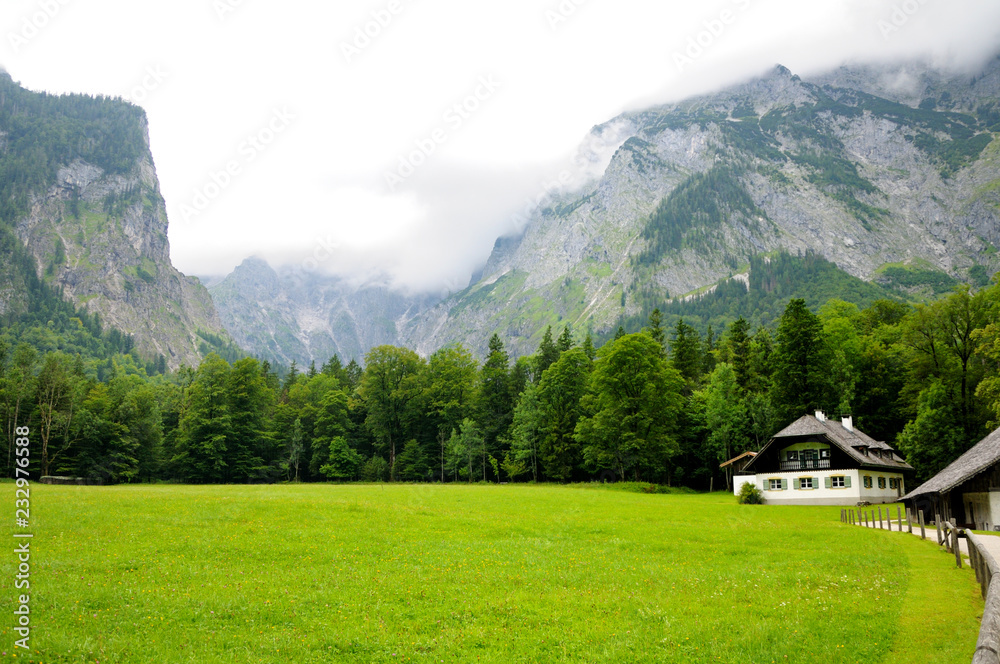 Beautiful white house with black roof and fresh green lawn. Trees grow along the lawn. Mountains in the background. Summer day.