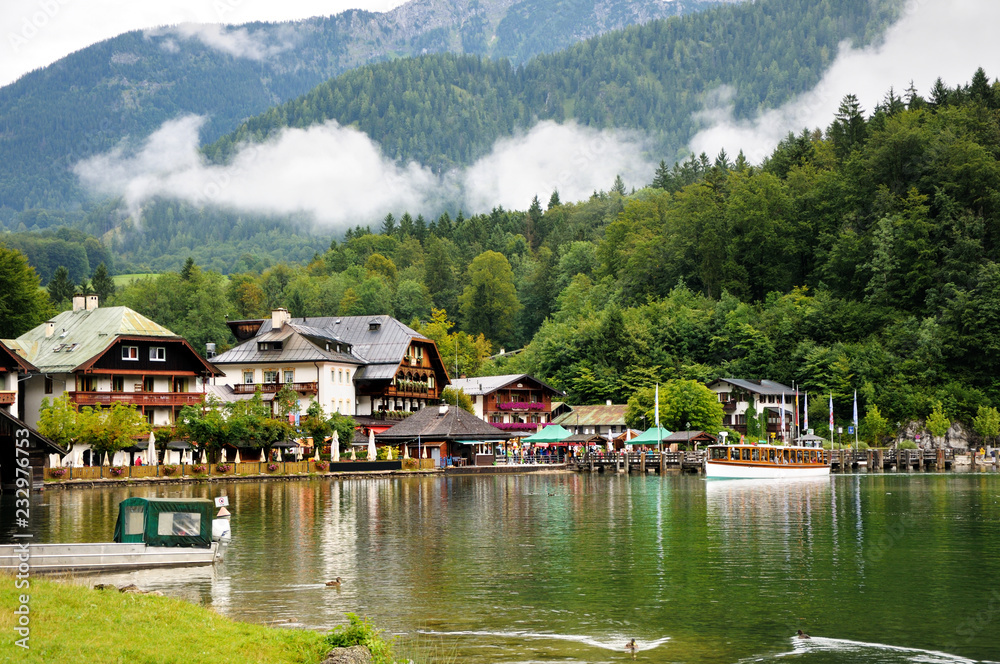 Houses and pier on the shore of Konigssee lake. Mountains with clouds in the background. Bavaria, Germany.